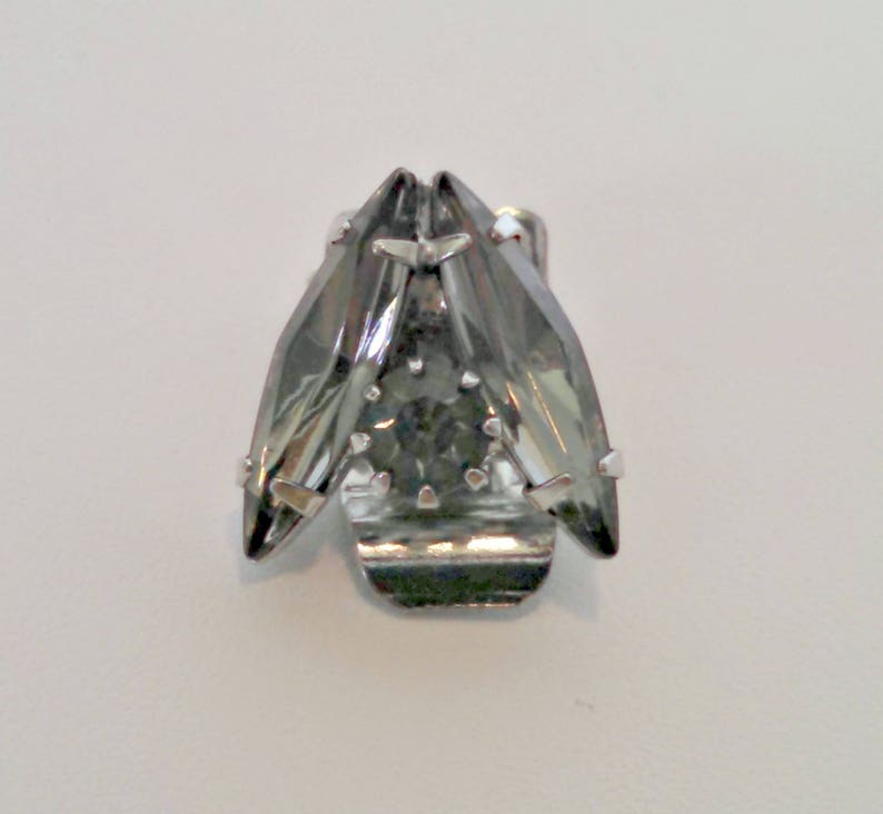 May include: A silver-toned brooch with a dark gray crystal in the center. The crystal is surrounded by smaller, faceted crystals.