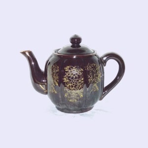 May include: A brown ceramic teapot with a gold floral design. The teapot has a lid and a spout.