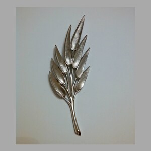May include: A silver-toned brooch in the shape of a stylized leaf with multiple branches and leaves.