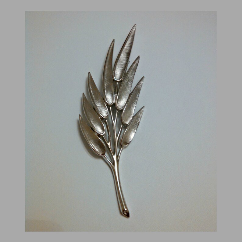 May include: A silver-toned brooch in the shape of a stylized leaf with multiple branches and leaves.