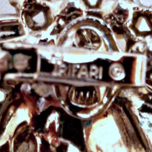 May include: Close-up of a silver-toned metal brooch with a floral design. The back of the brooch has the word "TRIFARI" and a copyright symbol.