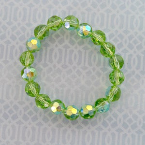 K&ouml;nnte beinhalten: Ein gr&uuml;nes Kristall-Armband mit schillernden Facetten. Das Armband besteht aus runden Perlen und ist etwa 18 cm lang.