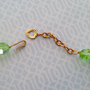 K&ouml;nnte beinhalten: Eine gr&uuml;ne Glasperlenkette mit einem goldenen herzf&ouml;rmigen Verschluss und einer goldenen Kettenverl&auml;ngerung.