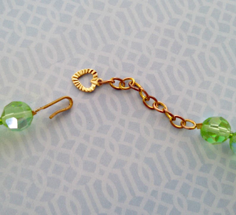 K&ouml;nnte beinhalten: Eine gr&uuml;ne Glasperlenkette mit einem goldenen herzf&ouml;rmigen Verschluss und einer goldenen Kettenverl&auml;ngerung.