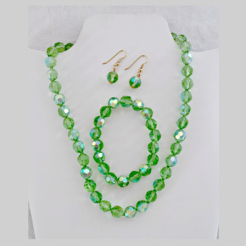 K&ouml;nnte beinhalten: Ein gr&uuml;nes Kristall-Halsketten-, Armband- und Ohrring-Set. Die Halskette und das Armband bestehen aus facettierten gr&uuml;nen Kristallperlen. Die Ohrringe sind klein und haben eine Tropfenform.