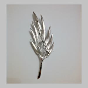 May include: Silver-toned leaf-shaped brooch with a pin and catch on the back.