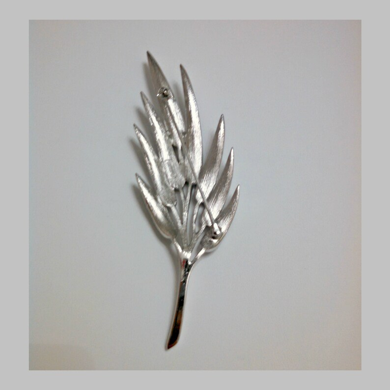 May include: Silver-toned leaf-shaped brooch with a pin and catch on the back.