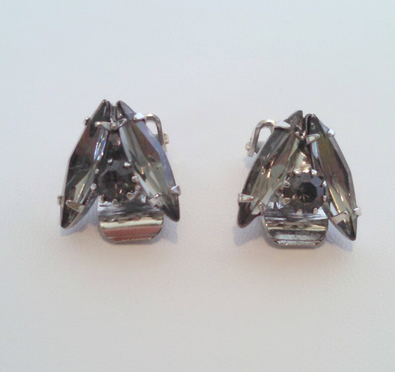 May include: A pair of silver tone clip-on earrings with a cluster of dark gray rhinestones.