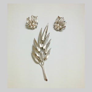 May include: A silver tone brooch and earrings set featuring a leaf design with faux pearls. The brooch is shaped like a branch with multiple leaves.