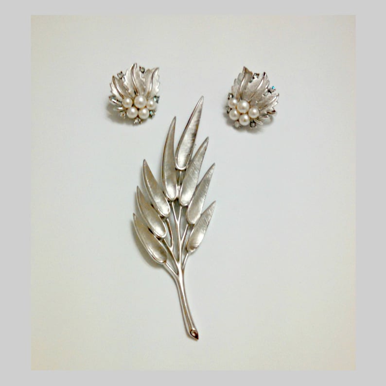 May include: A silver tone brooch and earrings set featuring a leaf design with faux pearls. The brooch is shaped like a branch with multiple leaves.