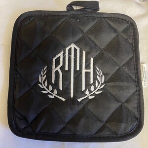 Può includere: Presa pentola imbottita nera con un monogramma bianco delle lettere "RTH" circondato da una ghirlanda di foglie.