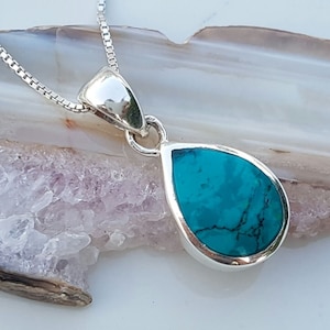 May include: A silver teardrop pendant necklace with a turquoise gemstone. The pendant is set in a silver bezel and hangs from a silver chain.