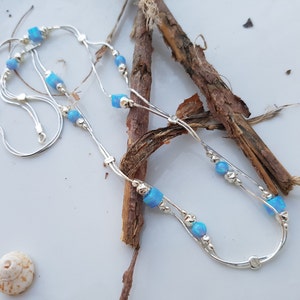 May include: A silver chain necklace with two strands and blue opal beads. The necklace is displayed on a wooden surface.