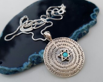 May include: A silver necklace with a round pendant featuring a Star of David with a turquoise stone in the center. The pendant is surrounded by Hebrew text.