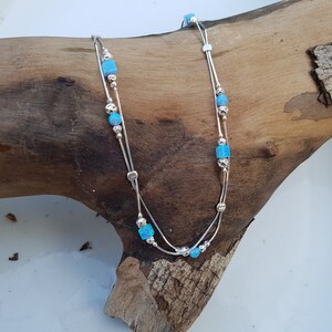 May include: A silver anklet with two delicate chains and blue opal beads. The anklet is displayed on a wooden surface.