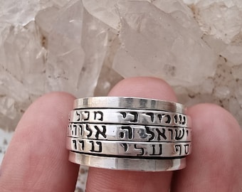 May include: A silver ring with multiple bands, each engraved with Hebrew text. The ring has a polished finish and a classic design. The bands are stacked together, creating a unique and eye-catching piece of jewelry.