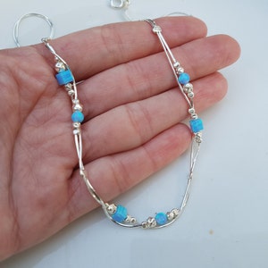 May include: A silver chain anklet with two strands and small silver beads. The anklet has five blue opal stones, four of which are square and one is round.