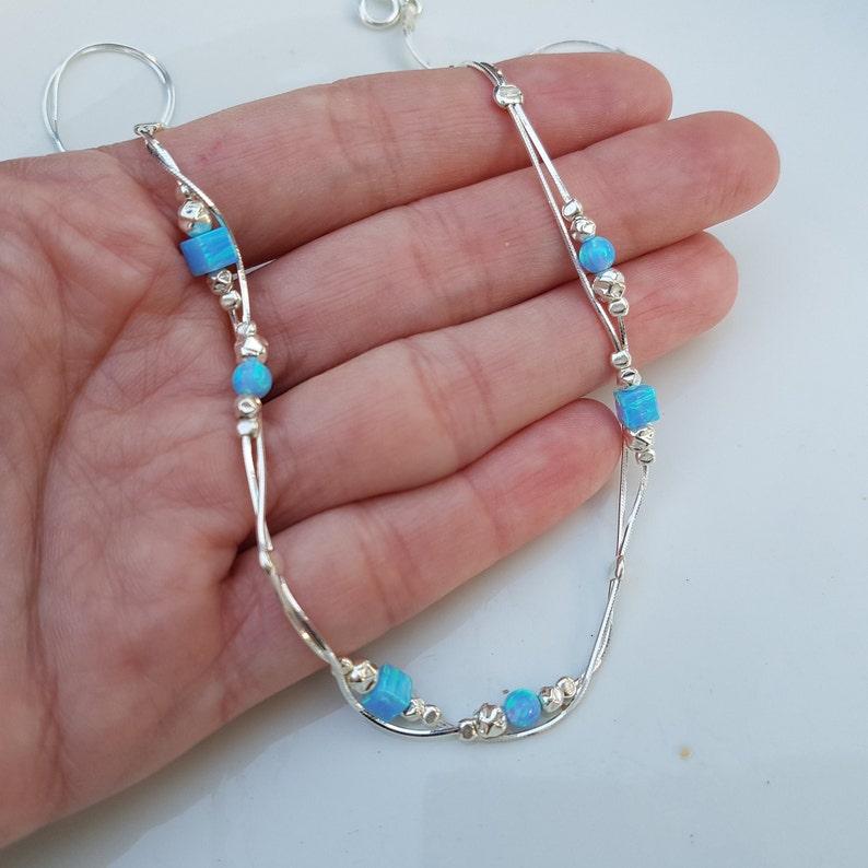 May include: A silver chain anklet with two strands and small silver beads. The anklet has five blue opal stones, four of which are square and one is round.