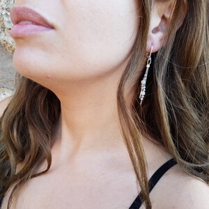 May include: A silver dangle earring with multiple small round beads hanging from a thin chain.