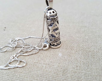 May include: A silver necklace with a pendant shaped like a small silver cylinder. The cylinder is decorated with a Star of David design and Hebrew lettering.