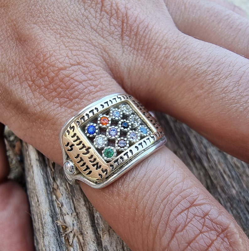 May include: A silver ring with a gold inlay featuring a square design with Hebrew text and colorful gemstones.