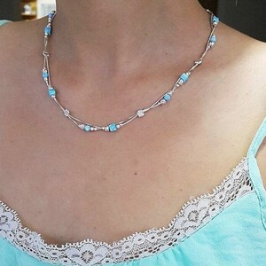 May include: A silver necklace with a delicate chain and small, light blue square beads.