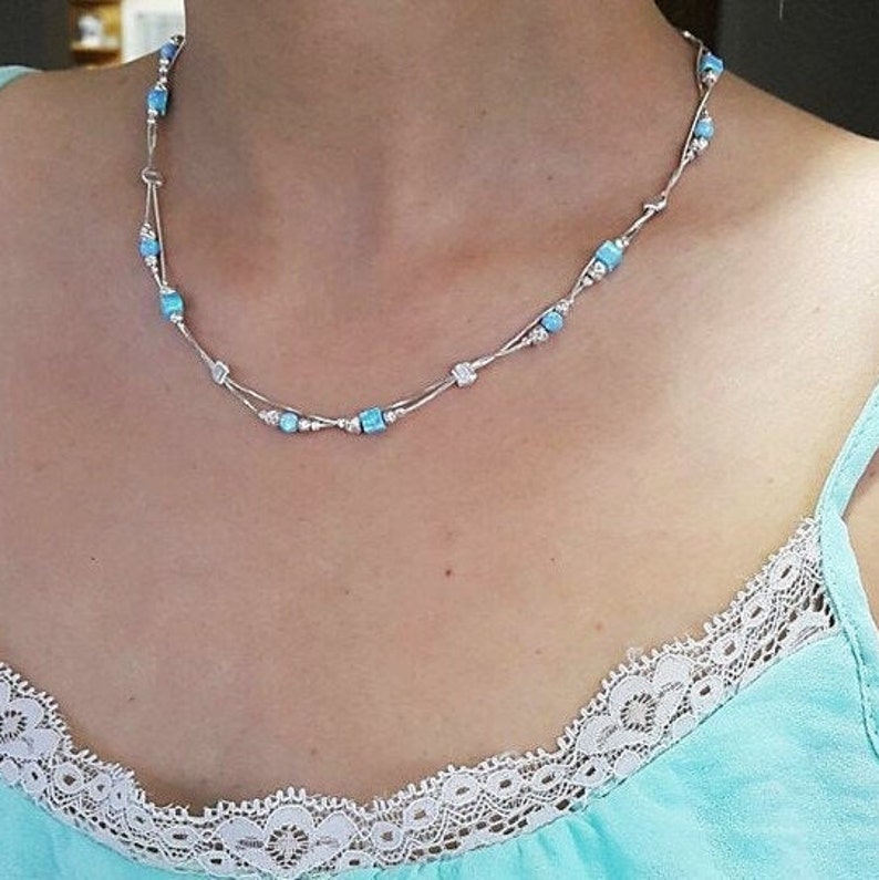 May include: A silver necklace with a delicate chain and small, light blue square beads.