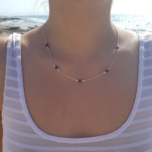 May include: A silver necklace with small green and silver beads. The necklace is on a person's neck.