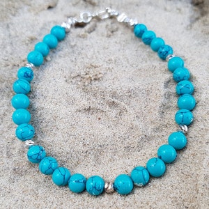 Puede incluir: Un brazalete de cuentas azul turquesa con un cierre plateado. El brazalete est&aacute; hecho de cuentas redondas y est&aacute; enhebrado en una cadena plateada.