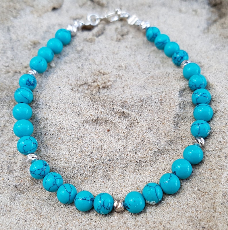Puede incluir: Un brazalete de cuentas azul turquesa con un cierre plateado. El brazalete est&aacute; hecho de cuentas redondas y est&aacute; enhebrado en una cadena plateada.