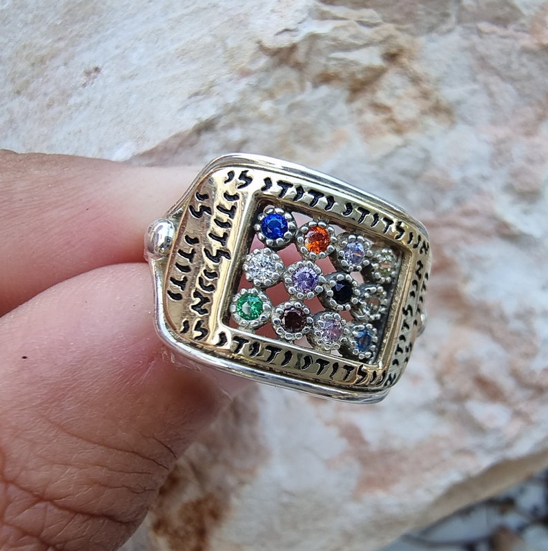 May include: A silver and gold ring with a square design featuring a grid of colorful gemstones and Hebrew lettering.