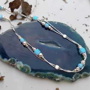 May include: A silver chain necklace with two strands and blue opal beads. The necklace is on a blue and green agate surface.