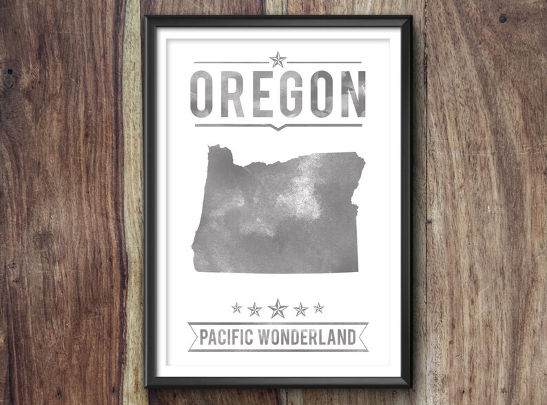 May include: Framed print featuring the state of Oregon in a watercolor style, with the state name above and "Pacific Wonderland" below. The artwork is in shades of gray and white, set against a wooden background.