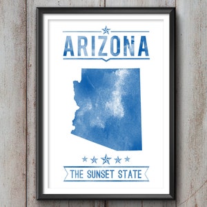 May include: Framed print featuring a blue watercolor map of Arizona on a white background. The word "ARIZONA" is above the map, and "THE SUNSET STATE" is below. The print is in a black frame.
