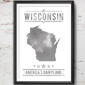 May include: Framed print featuring a gray watercolor map of Wisconsin, with the state name above and "America's Dairyland" below. The artwork is set against a white background and framed in black.