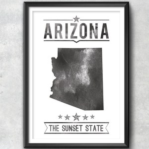 May include: Black and white framed print featuring the state of Arizona. The word "ARIZONA" is printed above the state outline, and "THE SUNSET STATE" is printed below. The print has a watercolor effect.