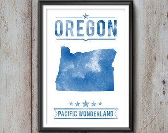 May include: Framed print featuring a blue watercolor map of Oregon, with the state name above and "PACIFIC WONDERLAND" below. The artwork is set against a white background, framed in black, and mounted on a wooden wall.
