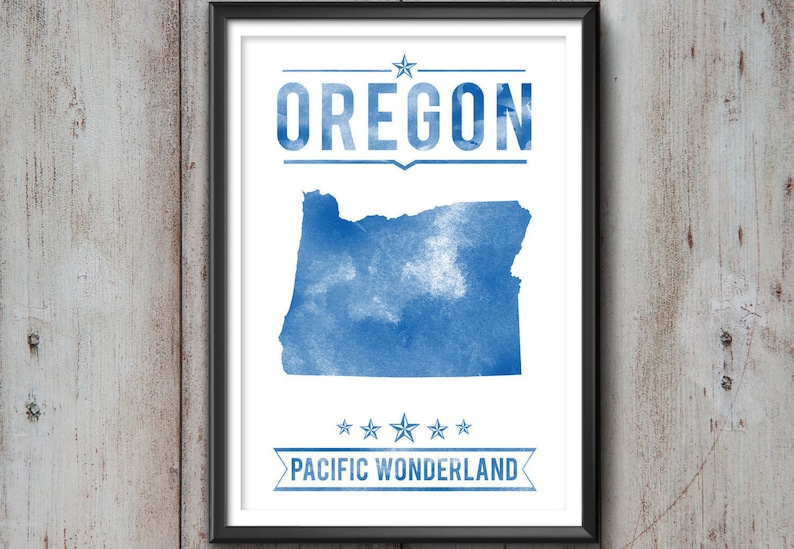 May include: Framed print featuring a blue watercolor map of Oregon, with the state name above and "PACIFIC WONDERLAND" below. The artwork is set against a white background, framed in black, and mounted on a wooden wall.