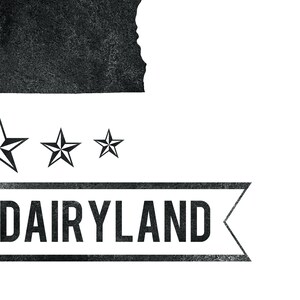 May include: A black and white graphic design featuring the word "DAIRYLAND" in a rectangular banner with a textured appearance. Above the banner are three stars and a silhouette of a state.