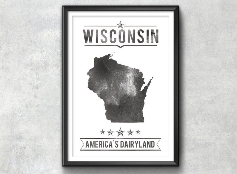 May include: Framed art print featuring a watercolor-style map of Wisconsin in shades of gray. The word "WISCONSIN" is printed above the map, and "AMERICA'S DAIRYLAND" is printed below, with stars and banners.