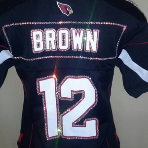 May include: A black football jersey with the name "BROWN" and the number "12" on the back, both decorated with rhinestones.