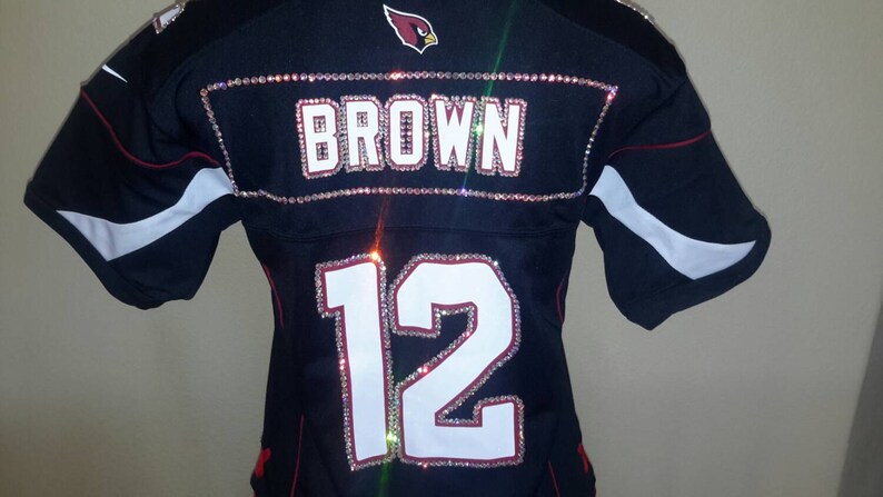 May include: A black football jersey with the name "BROWN" and the number "12" on the back, both decorated with rhinestones.