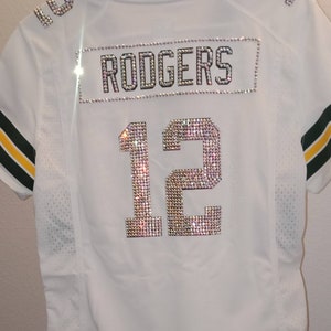 Puede incluir: Jersey blanco con ribetes verdes y amarillos. El n&uacute;mero 12 y el nombre "RODGERS" est&aacute;n escritos en pedrer&iacute;a.