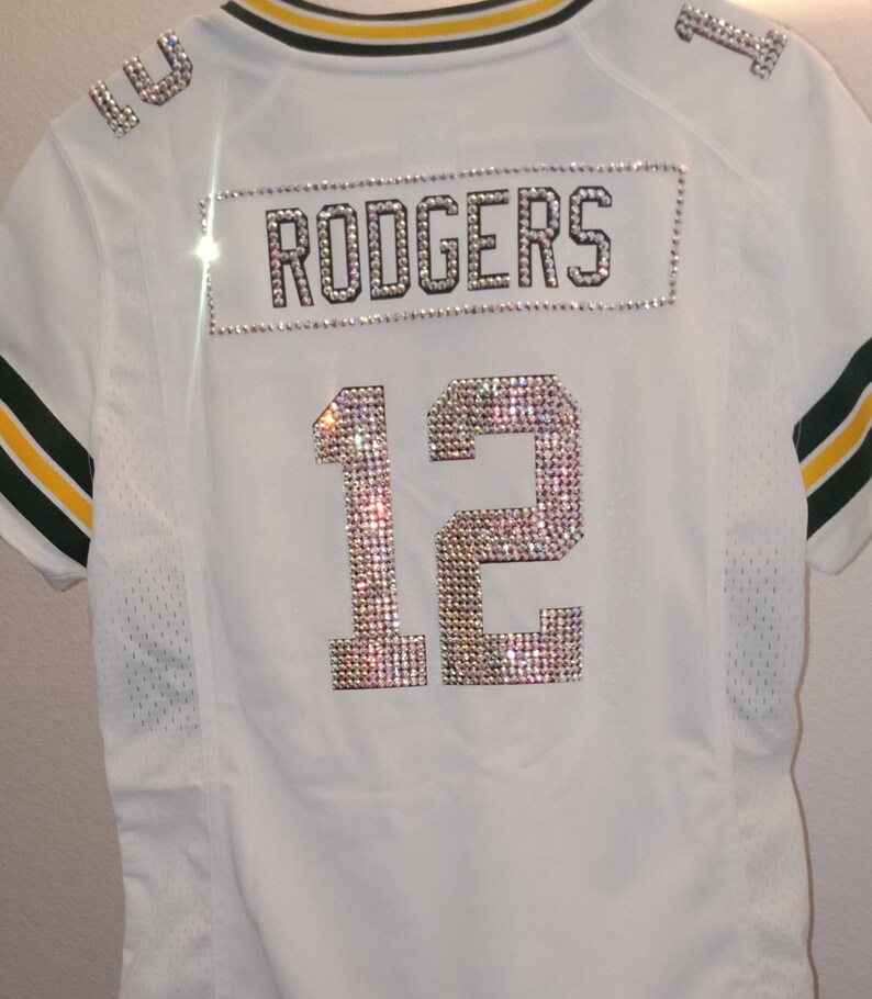 Puede incluir: Jersey blanco con ribetes verdes y amarillos. El n&uacute;mero 12 y el nombre "RODGERS" est&aacute;n escritos en pedrer&iacute;a.