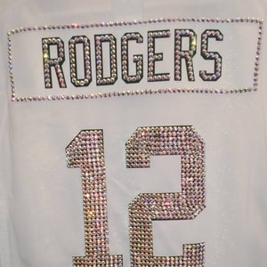 Puede incluir: Jersey blanco con el nombre "RODGERS" y el n&uacute;mero "12" en pedrer&iacute;a.