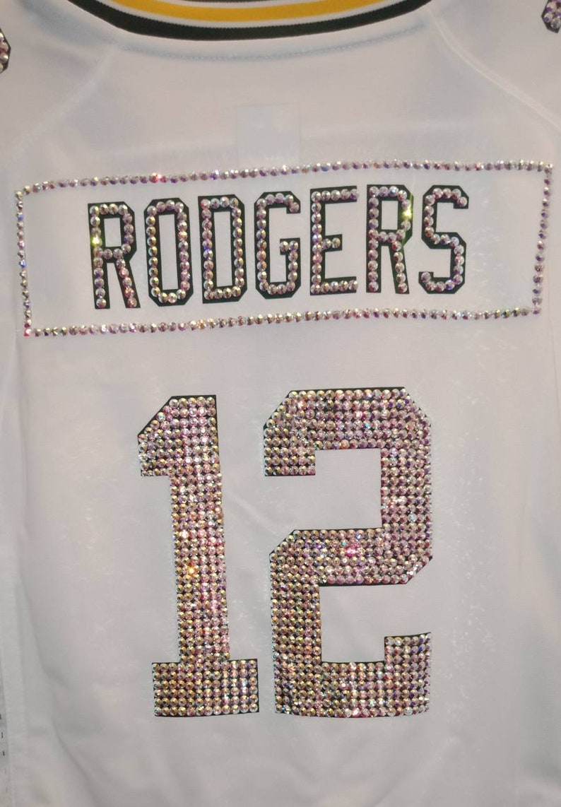 Puede incluir: Jersey blanco con el nombre "RODGERS" y el n&uacute;mero "12" en pedrer&iacute;a.