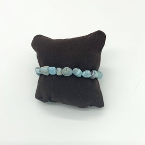 May include: A light blue gemstone bracelet with a brown velvet cushion background.