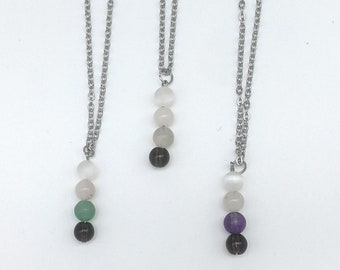 May include: Three silver necklaces with different colored beads. The necklaces have a silver chain and four beads each. The beads are white, black, green, and purple.