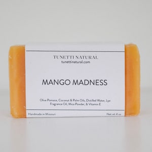 May include: A bar of mango-scented soap with a white label that reads "TUNETTI NATURAL, tunettinatural.com, MANGO MADNESS, Olive Pomace, Coconut & Palm Oils, Distilled Water, Lye, Fragrance Oil, Mica Powder, & Vitamin E, Handmade in Missouri, Net wt 4 oz".