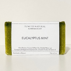 May include: A bar of green soap with a white label that reads "TUNETTI NATURAL tunettinatural.com EUCALYPTUS MINT Olive Pomace, Coconut & Palm Oils, Distilled Water, Lye Eucalyptus & Peppermint Essential Oils, Chlorella Powder, & Vitamin E Handmade in Missouri Net wt 4 oz"